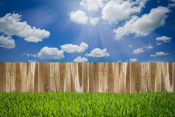 Wooden fence on green grass field with clouds in blue sky and sun light. Nature background concept.