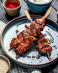 top view of grilled chicken skewers with soy sauce on a plate on wooden background