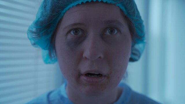 Crazy stressed woman with face and dental injuries in medical uniform in a hospital is scared and interested in looking somewhere. Mental disease patient. Suffering from mental disorder.