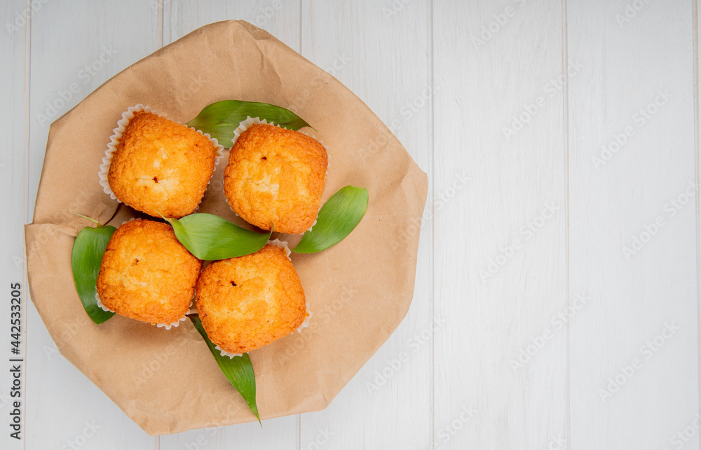 Aufkleber top view of muffins with green leaves on a craft brown paper on white rustic background with copy sp