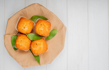 top view of muffins with green leaves on a craft brown paper on white rustic background with copy space