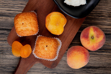 top view of muffins with dried apricots on wooden cutting board and fresh peaches on rustic background