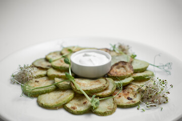 closeup of fried zucchini slices with sour cream on plate on white background