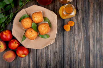 top view of muffins with green leaves on craft brown paper with fresh ripe nectarines and peach jam in a glass jar on rustic wooden background with copy space