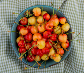 top view of ripe rainier cherries in a bowl on plaid fabric background