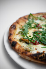 closeup of seafood pizza with shrimp, mussels and arugula on white background