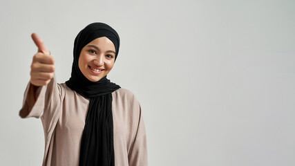 Cheerful young arabic woman in hijab showing thumb up