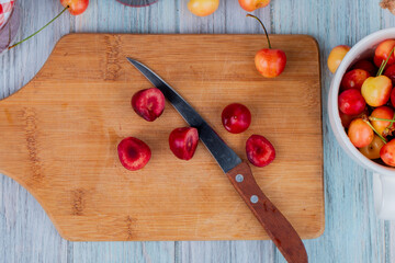 top view of slices of red ripe cherry on a wooden cutting board with a kitchen knife on rustic background