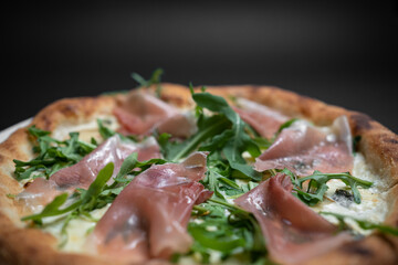 closeup of italian pizza with prosciutto, arugula and cheese on black background