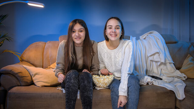 Two teenage girls celebrating victory in sports game watching on TV at night