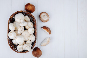 top view of white mushrooms  in a wicker basket on white wooden background with copy space