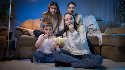 Naklejka premium Group of people eating popcorn while watching movie or TV show in living room at night.