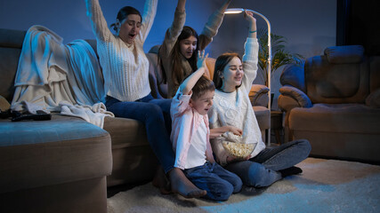 Happy family celebrating victory of sports team watching TV match at night.