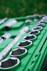 Obraz premium Chrome mechanics tools set. Close-up photo of a set of sockets with a screwdriver and a ratchet in a green plastic case against a background of green grass. Auto tool.