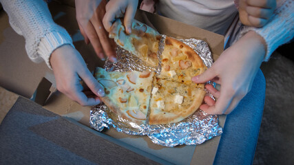Closeup of friends taking pizza slices from cardboard box while watching TV at night.