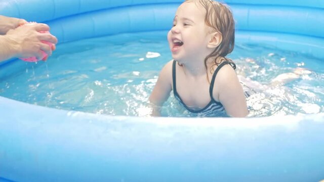 A little girl in an inflatable pool. Backyard of the house, outdoor, rest in nature. Happiness, joy, smile, funny children. an active lifestyle. Dad's playing with his daughter.