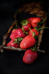 Ripe red strawberries scattered from wicker basket on dark background