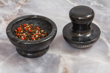 Black stone bowl with peppercorn on gray background.