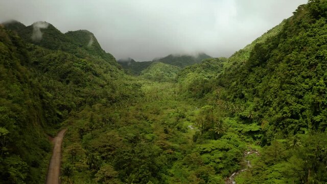 Mountains covered rainforest, trees and river in cloudy weather, aerial drone. Camiguin, Philippines. Mountain landscape on tropical island with mountain peaks covered with forest. Slopes of mountains