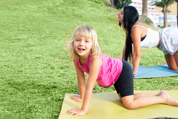 Cute happy little girl in sportswear smiling at camera while while exercising on seaside