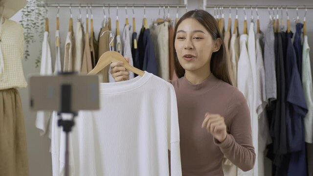 Young bautiful woman selling her clothing. She using smartphone to live streaming with customer.