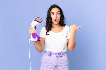 hispanic pretty woman looking astonished in disbelief and holding an iron steam