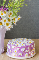 Lilac birthday cake decorated with daisies on a wooden background