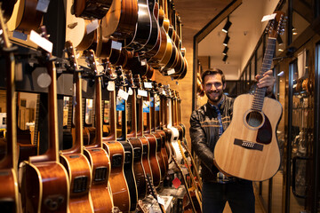 Portrait of talented caucasian musician in leather jacket standing in music shop and holding...