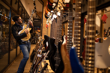 Proud young rocker musician in leather jacked playing electric guitar in music shop.