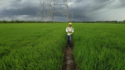 An energy engineer in special clothes inspects a power line using data from electric sensors on a tablet.