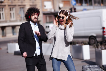 Young business colleagues dancing together with headphones after work. Happy friends jumping and...