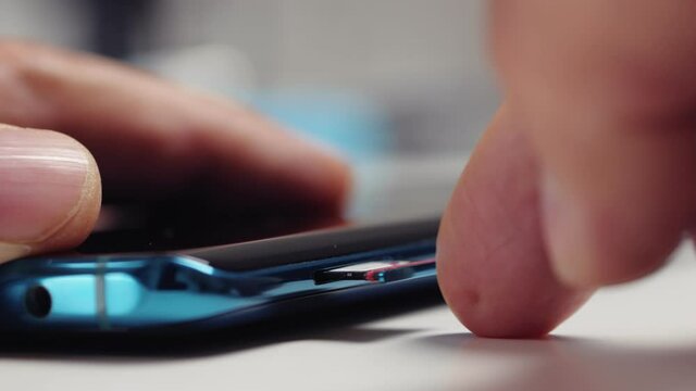 Close-up of a man's hand inserting a tray with two nano-SIM cards into a modern smartphone
