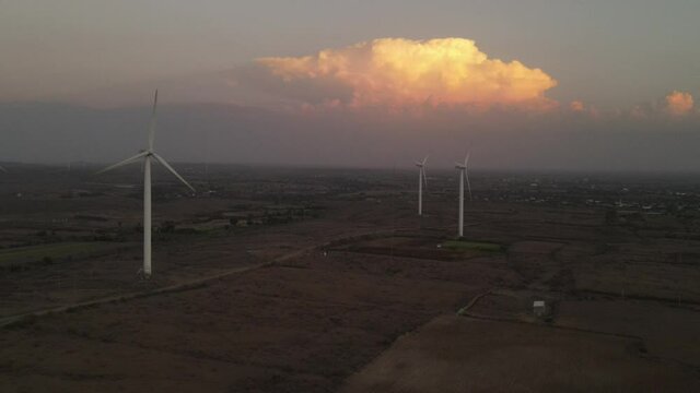Large wind turbines with blades in field aerial view bright orange sunset