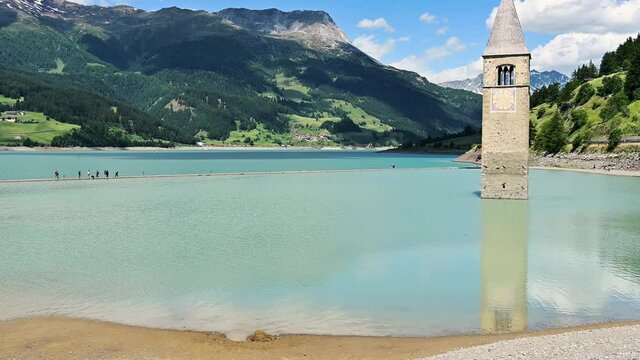 Curon, Italy, June 2021. Amazing tilt footage on a beautiful summer day of the old bell tower of Curon (Graun) emerging from the waters of Lake Resia, South Tyrol, Italy.