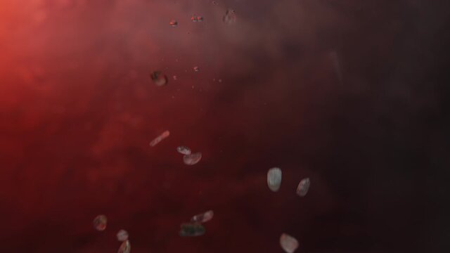 Close up of rocks falling into fish tank in slow motion, bubbles flow up, textured background with red/orange lighting, shallow depth of field