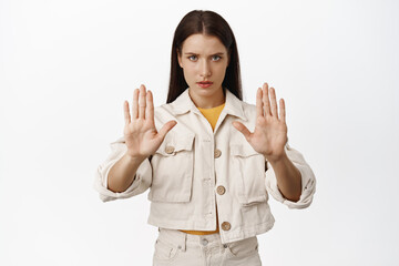 Stop. Serious and confident brunette woman raising hands in taboo sign, furrow eyebrows, give...