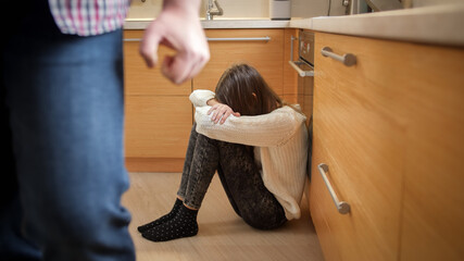Angry father with clenched fist walking away from crying daughter sitting on kitchen floor. Concept of domestic violence and family aggression. - obrazy, fototapety, plakaty