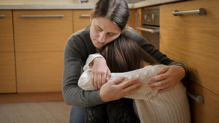 Young mother comforting and calming her daughter crying on floor at kitchen. Concept of domestic...