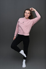 Full length studio portrait of cute caucasian girl in pink sweater and black pants with smile posing on gray background