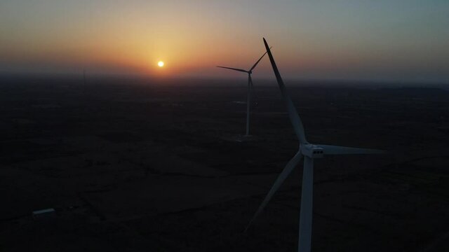 Large wind turbines with blades in field aerial view bright orange sunset