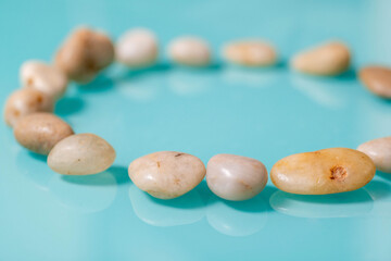A circle of sea pebbles close-up on a turquoise glossy background.