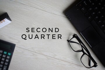 Top view of calculator, glasses, laptop and desk calendar on wooden table with text SECOND QUARTER....