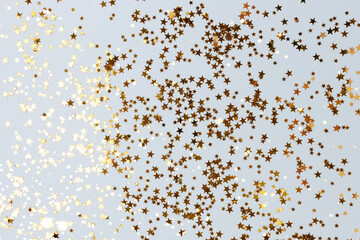 Bright gold glittering stars confetti scattered on a blue pastel background.