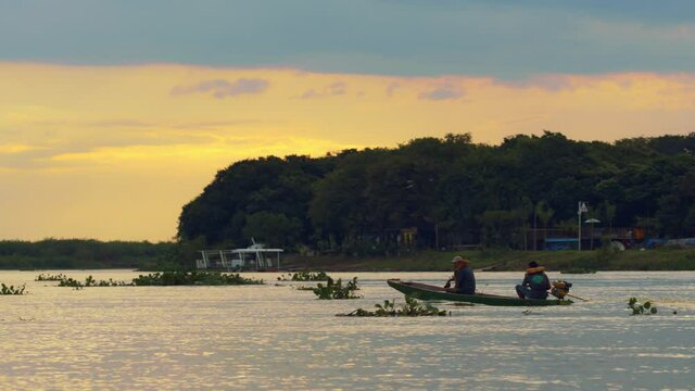 A small motorboat crosses a wide river during a golden sunset or sunrise