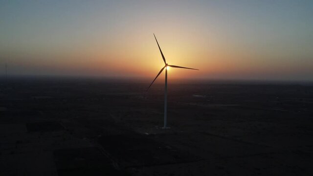 Large wind turbines with blades in field aerial view bright orange sunset