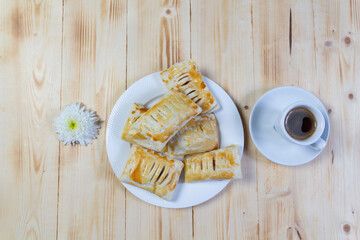 Small cup of black coffee, cookies on white plate,  daisy chrysanthemum flower on wooden table