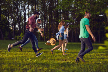 Group of happy young people running on grass in summer park. Youth on vacation.