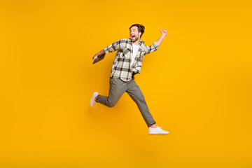 Fototapeta na wymiar Full size profile side photo of young man happy positive smile jump up go run hold laptop isolated over yellow color background