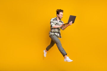 Full body profile side photo of young man happy positive smile jump use laptop isolated over yellow color background