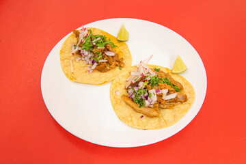 Tacos with corn flour tortillas with lots of coriander, red onion, radishes and stewed chicken on a white plate